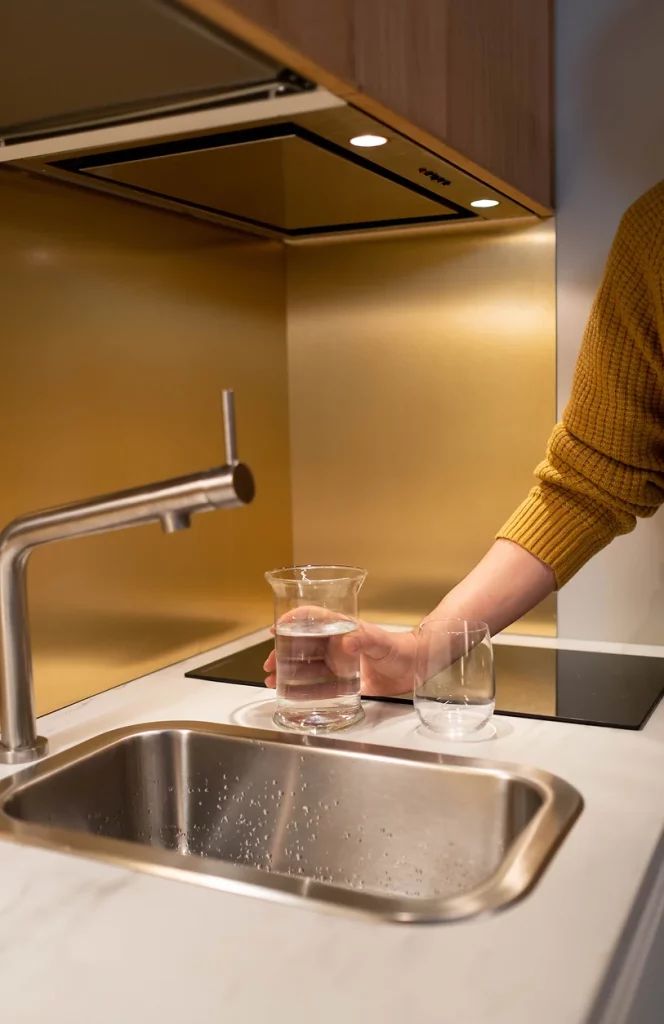 Remplissage d’une carafe d’eau purifiée directement au robinet, illustrant l’efficacité d’un purificateur d’eau domestique dans une cuisine moderne.