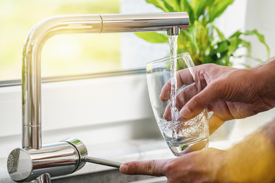 Main remplissant un verre d’eau filtrée au robinet dans une cuisine, illustrant une consommation écoresponsable