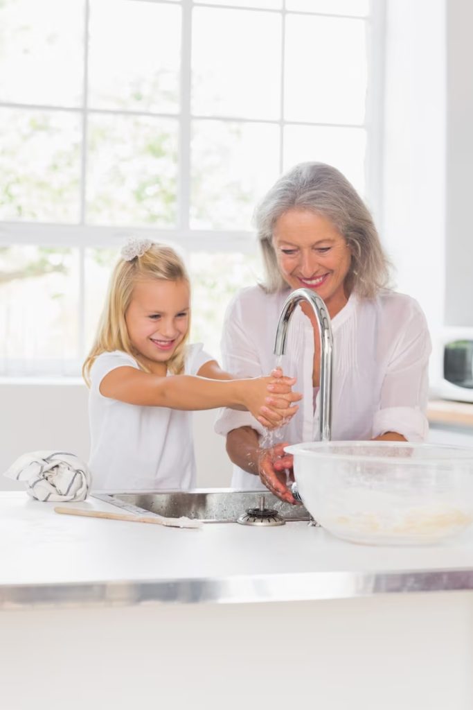 Grand-mère et enfant se lavant les mains ensemble à l’évier avec de l’eau filtrée, mettant en avant l’importance de la purification de l’eau au quotidien.